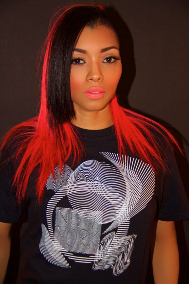May include: A woman with long black and red hair is wearing a black t-shirt with a white geometric design.