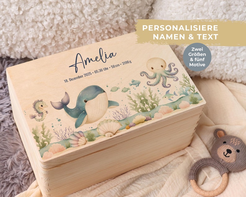 May include: A light wooden box with a hinged lid, decorated with an underwater scene featuring a whale, octopus, and seahorse. The box has the name "Amelia" and birth details printed on the lid. The text "PERSONALISE NAMEN & TEXT" is also visible.