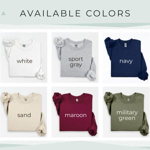 Pu&ograve; includere: Esposizione di sei felpe girocollo in vari colori: bianco, grigio sportivo, blu navy, sabbia, bordeaux e verde militare. Il testo "AVAILABLE COLORS" &egrave; nella parte superiore dell'immagine.