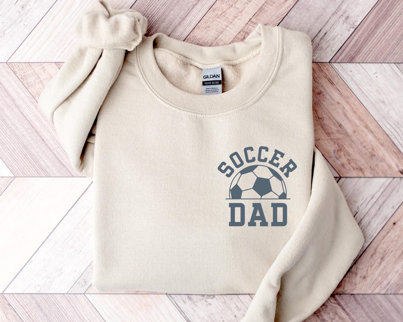 Pu&ograve; includere: Una felpa color crema con la scritta "SOCCER DAD" stampata in grigio, insieme a una grafica di pallone da calcio. La felpa &egrave; realizzata in un materiale morbido e ha uno scollo tondo.