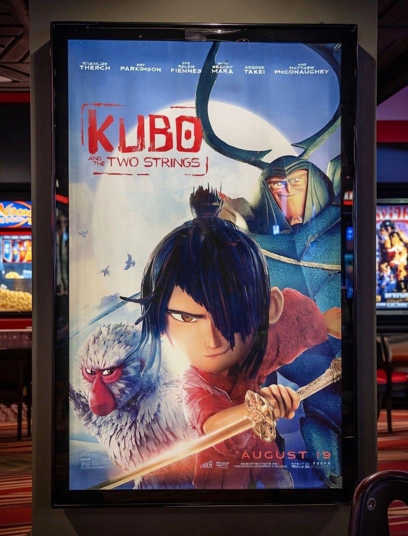 K&ouml;nnte beinhalten: Kinoplakat f&uuml;r den Film "Kubo - Der Zauber der zwei Saiten". Das Poster zeigt eine junge Figur mit schwarzen Haaren und einem Schwert, einen Affen und eine gro&szlig;e gepanzerte Figur. Der Titel ist rot, mit dem Erscheinungsdatum "19. August".