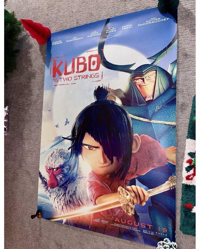 K&ouml;nnte beinhalten: Ein Filmplakat f&uuml;r "Kubo - Der tapfere Samurai" mit einem jungen Mann mit Schwert, einem Affen und einer gro&szlig;en blauen Figur. Das Plakat zeigt den Filmtitel und das Erscheinungsdatum, 19. August.