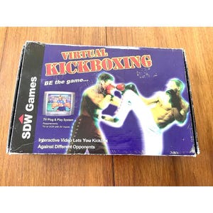 May include: A rectangular box for the video game "Virtual Kickboxing" by SDW Games. The box is primarily purple with illustrations of two kickboxers. Text includes "BE the game..." and "Interactive Video Lets You Kickbox Against Different Opponents."