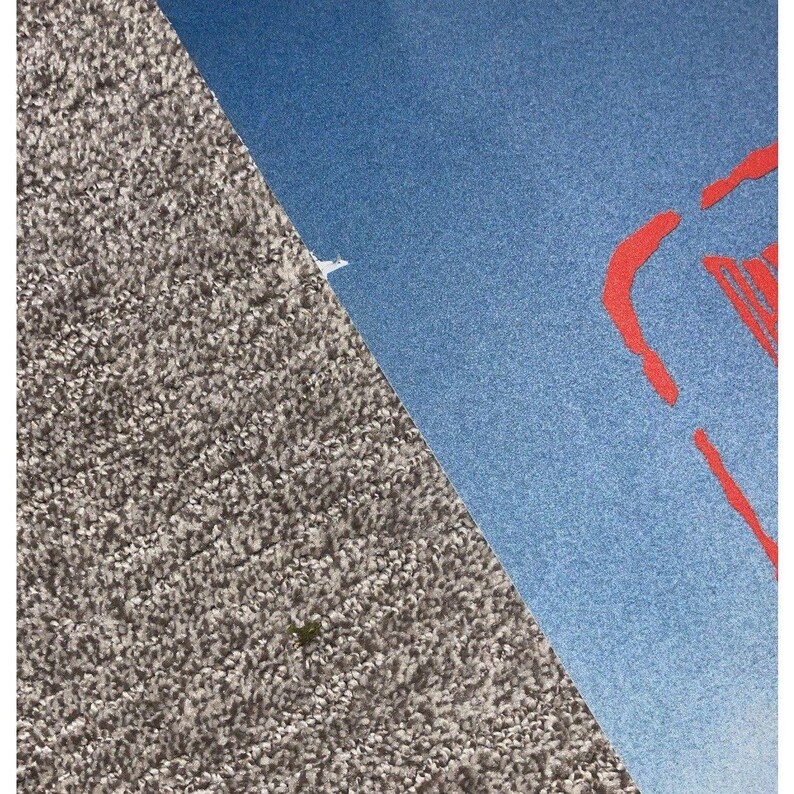 K&ouml;nnte beinhalten: Diagonale Komposition mit einer strukturierten, grauen Oberfl&auml;che und einer blauen Oberfl&auml;che mit roten abstrakten Formen. Eine kleine wei&szlig;e Form ist auf der blauen Oberfl&auml;che sichtbar. Das Bild hat eine moderne, grafische Design&auml;sthetik.