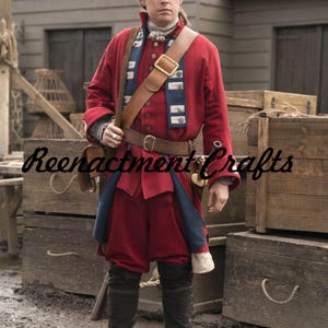 May include: A red historical costume with a brown leather belt and shoulder strap. The costume includes a long-sleeved jacket, knee-length breeches, and a blue and white sash. The text "Reenactment Crafts" is visible.
