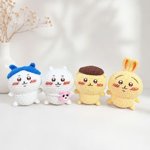 May include: Four small, round, crocheted plush figures arranged in a row. The first is white with a blue cap, the second is white with a pink flower, the third is yellow with a brown cap, and the fourth is a yellow rabbit with long ears.