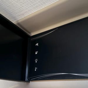 Puede incluir: Un panel de control negro con iconos y texto blancos, probablemente para un vehículo o una autocaravana. Los iconos incluyen un grifo, un indicador de combustible, una bombilla, un termómetro, agua y un botón de encendido/apagado. El panel tiene un elemento de diseño blanco curvo.
