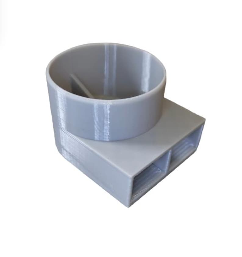 May include: A light grey 3D-printed object. It has a cylindrical top and a rectangular base with two openings. The cylindrical part has a divider inside. The object is made of plastic and shows layer lines from the printing process.