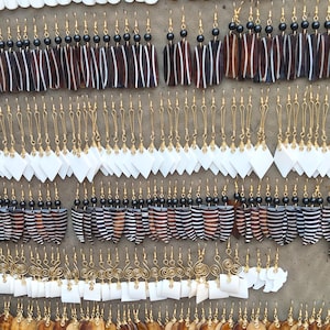 May include: A large collection of dangling earrings featuring various shapes including leaf, rectangular, diamond, circular, and spiral designs. The earrings are crafted from white and brown materials, accented with black beads and gold-toned metal hooks.