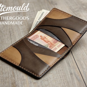 Pode incluir: Carteira de couro artesanal em tons de castanho e bege, com um design geométrico único. A carteira está aberta, revelando dinheiro e um cartão de crédito. O texto "Ytcmould LEATHERGOODS HANDMADE" é visível.
