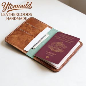 Könnte beinhalten: Geöffnete braune Leder-Passhülle mit hellgrünem Innenraum und weißen Nähten. Ein weinroter Reisepass befindet sich im Inneren. Der Text "Ytcmould LEATHERGOODS HANDMADE" befindet sich oben links.