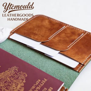May include: Brown leather passport holder with white stitching and card slots. The holder is open, revealing a burgundy passport and white cards. The text "Ytcmould LEATHERGOODS HANDMADE" is visible in the upper left corner.