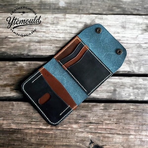 May include: Handmade leather wallet with a bi-fold design. The wallet features a combination of black, brown, and blue leather, with white stitching. The interior has multiple card slots. The logo "Leathergoods Ytcmould Handmade" is visible.