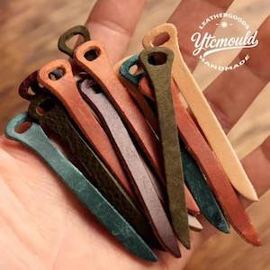 Könnte beinhalten: Eine Sammlung handgefertigter Lederwaren in verschiedenen Farben, darunter Grün, Braun und Beige. Die Artikel sind länglich mit einer Schlaufe an einem Ende. Der Text "LEATHERGOODS Ytcmould HANDMADE" ist oben rechts sichtbar.