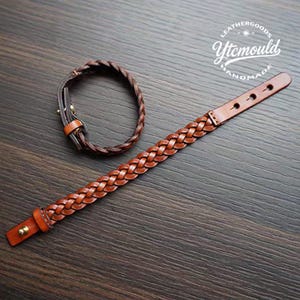 May include: Two brown leather bracelets. One is a braided style, and the other is a smaller, braided bracelet. Both bracelets have a buckle closure. The bracelets are on a dark wood surface. The logo "Leathergoods Ytemould Handmade" is in the upper right corner.