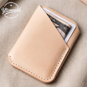 Può includere: Un porta carte in pelle color beige chiaro con un design piegato, bordi cuciti e una carta bianca e banconote piegate visibili all'interno. Il porta carte è fatto a mano e presenta il testo "LEATHERGOODS Ytcmould HANDMADE".