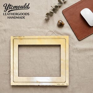 May include: A wooden frame with a rectangular cutout, labeled "XBC-02 7G" and "WVN251118IOR C4". The frame is on a neutral-toned fabric surface, with a brown leather mousepad and a white mouse. The top left corner has the text "Ytcmould LEATHERGOODS HANDMADE".