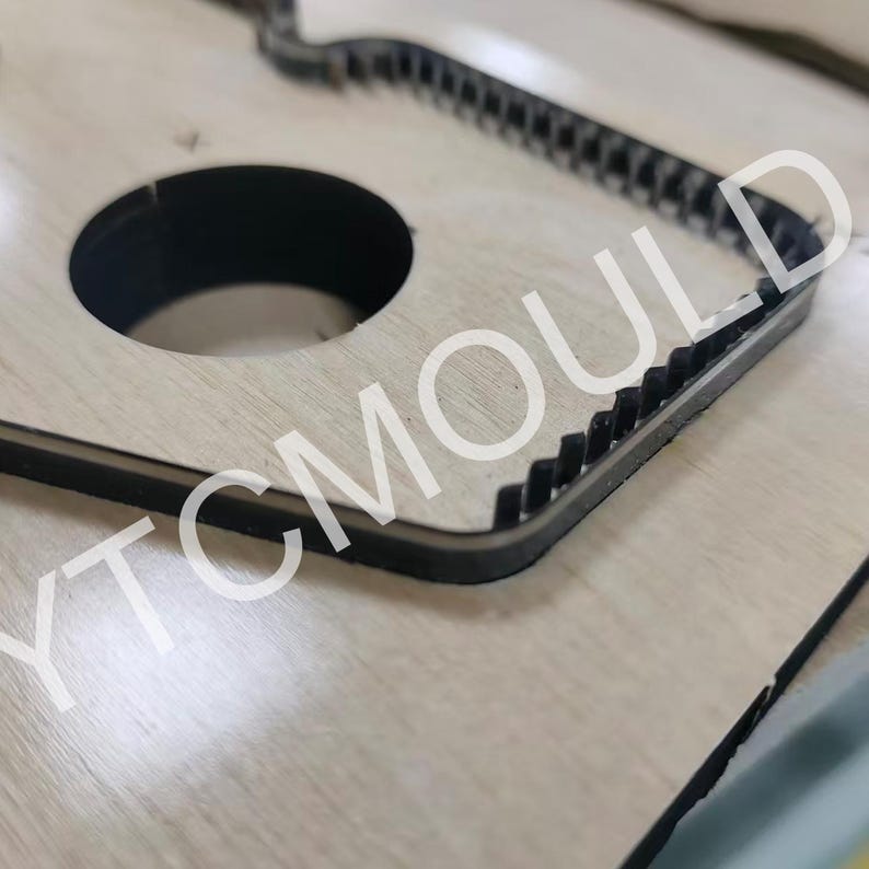 May include: A wooden die-cut with a circular cutout and a black, jagged edge. The text "YTCMOULD" is visible on the surface. The die-cut is likely used for crafting or manufacturing purposes.