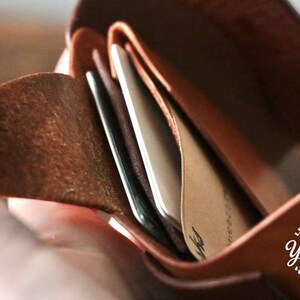 May include: Open brown leather wallet with several cards visible inside. The wallet is held open, showcasing the interior compartments and the cards within. The leather has a natural, textured appearance.