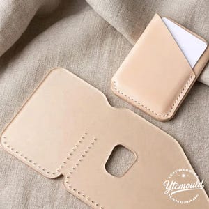 May include: A light beige leather card holder with a matching open wallet. The card holder is filled with white cards. The open wallet has a rectangular cutout. The items are handmade and stitched with a light beige thread.