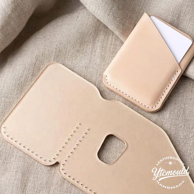 May include: A light beige leather card holder with a matching open wallet. The card holder is filled with white cards. The open wallet has a rectangular cutout. The items are handmade and stitched with a light beige thread.