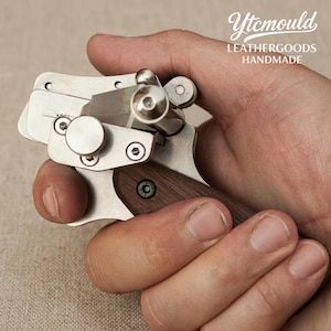 Puede incluir: Una herramienta de artesanía en cuero plateada y de madera sostenida en una mano. La herramienta tiene una cuchilla, un mango de madera y el texto "Ytcmould LEATHERGOODS HANDMADE".