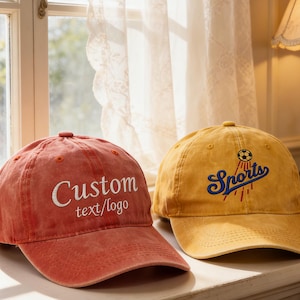May include: A red baseball cap with the white embroidered text Custom text/logo and a yellow baseball cap with a blue embroidered script word Sports and a small soccer ball graphic above it. Both caps feature a curved brim and a structured crown.