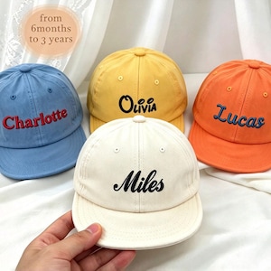 以下が含まれることがあります： 青、黄、オレンジ、クリーム色の4つの野球帽。それぞれにCharlotte、Olivia、Lucas、Milesという名前が刺繍されています。画像左上には「from 6months to 3 years」というテキストが表示されています。