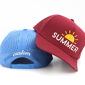 May include: Two baseball caps. One is a light blue with the word "custom" in white script on the back. The other is burgundy with the word "SUMMER" and a yellow sun graphic on the front. Both caps have a mesh design.