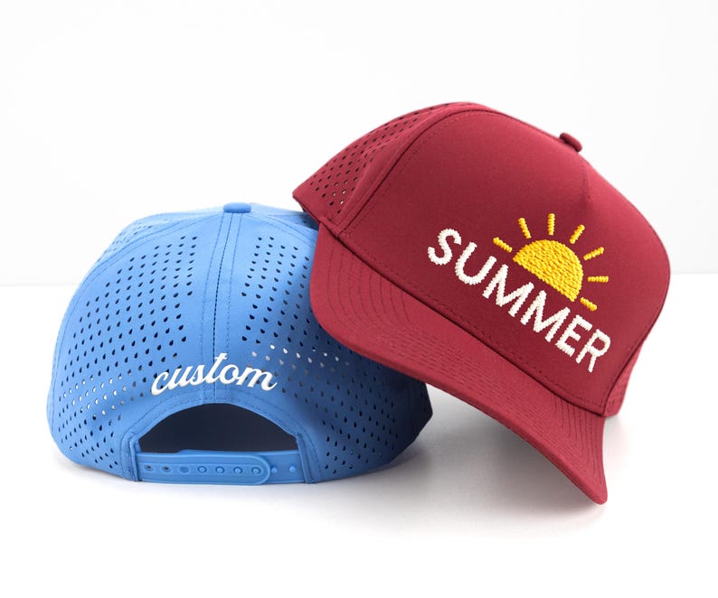 May include: Two baseball caps. One is a light blue with the word "custom" in white script on the back. The other is burgundy with the word "SUMMER" and a yellow sun graphic on the front. Both caps have a mesh design.