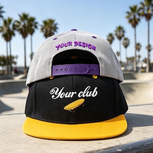 May include: A stacked pair of snapback caps. The top cap is light grey with purple text reading "YOUR DESIGN" and a purple plastic snap closure. The bottom cap is black with white cursive text reading "Your club" and a yellow graphic of a skateboard.