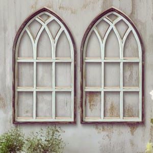 Könnte beinhalten: Zwei dekorative Wandregale in Form von Bogenfenstern. Jedes Regal hat eine verwitterte weiße Oberfläche mit einem dunkelbraunen Rahmen. Die Regale haben ein gitterartiges Design mit kleinen Ablagen zum Ausstellen von Gegenständen. Das Gesamtthema ist rustikal und vintage.