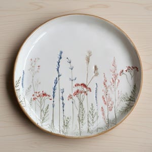 Op de afbeelding: Witte keramische serveerschaal met een verhoogd bloemmotief. De bloemen zijn in tinten rood, blauw en roze, met groen blad. De rand heeft een natuurlijke, lichtbruine kleur.