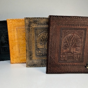 Può includere: Quattro diari in pelle nera, oro, grigio e marrone, ognuno con un disegno dell'albero della vita. I diari hanno bordi decorativi e chiusure in metallo. I diari sono in piedi.