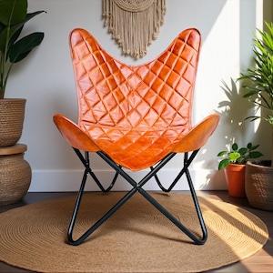 May include: An orange leather butterfly chair with a diamond-stitched pattern. The chair has a black metal frame and is set on a round jute rug. The chair is surrounded by potted plants, creating a cozy, bohemian vibe.