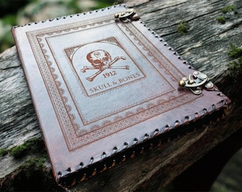 May include: A brown leather journal with the text "1912 SKULL & BONES" and a skull and crossbones emblem. The journal has decorative stitching along the edges and metal clasps. The cover features an embossed design.