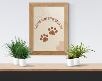 May include: A framed print with the text "Stay Paw-some Every Single Day" and paw prints. The print is in a wooden frame and is displayed on a wooden shelf with potted plants.