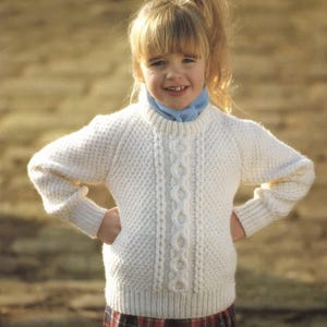 May include: A cream-colored, knitted sweater with a cable knit design down the center. The sweater has a ribbed collar, cuffs, and hem. The sleeves are long, and the overall style is classic and warm. The sweater is suitable for children.