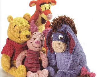 May include: A group of four crocheted plush toys featuring characters from Winnie the Pooh. The toys include Winnie the Pooh in yellow, Piglet in pink, Tigger in orange, and Eeyore in purple. Each toy has detailed facial features and is made with a textured yarn.