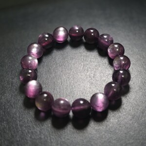 Peut inclure: Un bracelet composé de perles rondes et polies de couleur violette. Les perles présentent un effet œil de chat, avec une bande plus claire. Le bracelet est monté sur un cordon élastique transparent. Chaque perle mesure environ 1 cm de diamètre.