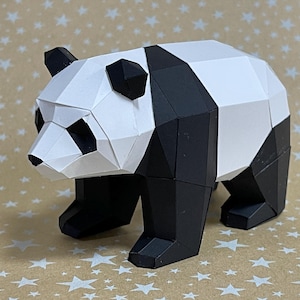 Peut inclure: Une sculpture géométrique en papier représentant un panda. Le panda est principalement blanc et noir, avec un design polygonal. Les oreilles, les pattes et des sections du corps sont noires, tandis que le visage et le dos sont blancs. Le panda est posé sur une surface à motifs d'étoiles.