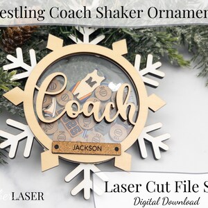 May include: A wooden wrestling coach shaker ornament in the shape of a snowflake. The ornament has a clear center filled with small wooden tokens and the word "Coach". A small rectangular tag reads "Jackson". The text "Laser Cut File SVG" is also visible.