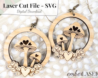 May include: A pair of laser cut wooden earrings featuring a mushroom design with hearts. The earrings are in the shape of a circle with a smaller circle inside. The mushrooms are detailed with hearts and a stem. The earrings are hanging from a silver hook.