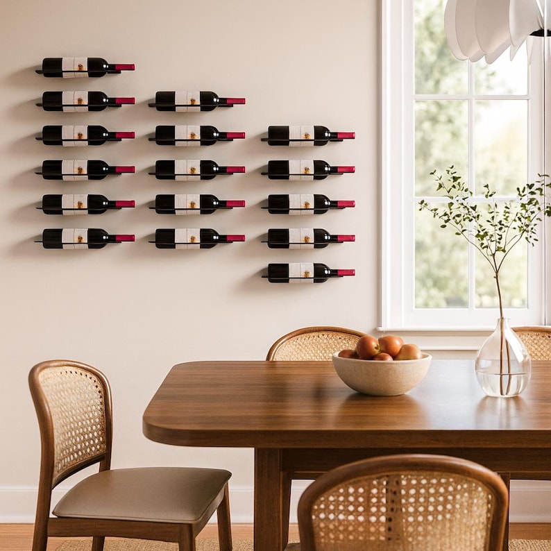 May include: A wall-mounted wine rack displaying several bottles of red wine. The bottles are black with white labels and red foil. The rack is mounted on a neutral-colored wall, with a dining table and chairs in the foreground.