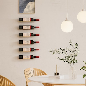 May include: A wall-mounted wine rack displaying six bottles of red wine. The bottles are arranged horizontally on individual gold-colored shelves. The wine bottles have red capsules and white labels. The rack is mounted on a light-colored wall, with a painting above.