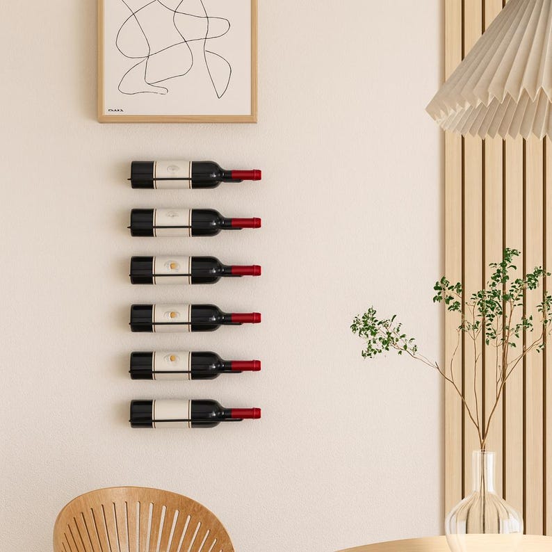 May include: A wall-mounted wine rack holding six bottles of red wine. The bottles are black with white labels and red corks. The rack is mounted on a cream-colored wall, with a framed abstract art print above.