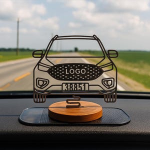 Könnte beinhalten: Ein Auto-förmiges Armaturenbrett-Dekoration mit dem Wort "LOGO" und der Nummer "38851" auf der Vorderseite. Die Dekoration ist schwarz und silber und steht auf einem Holzsockel. Der Hintergrund zeigt eine Straße und den Himmel.