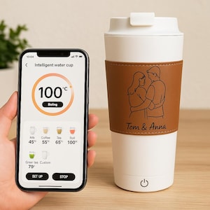May include: A white and brown smart travel mug with a leather band featuring a couple's illustration and the names "Tom & Anna". A smartphone displays the mug's temperature settings, showing 100°C. The mug has a power button.