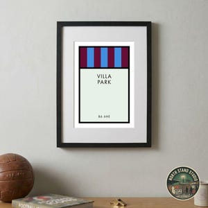 May include: A framed art print featuring a graphic design of Villa Park. The top section has vertical stripes in blue and maroon. The lower section is light cream with the text VILLA PARK and B6 6HE in black, enclosed in a black frame.