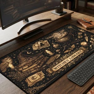 May include: A rectangular desk mat featuring a dark background with gold-toned illustrations of an owl, a pointed hat, stacked books, tarot cards, a cauldron, and candles. The text "WITCHES LIBRARY" is printed on a scroll-like banner.